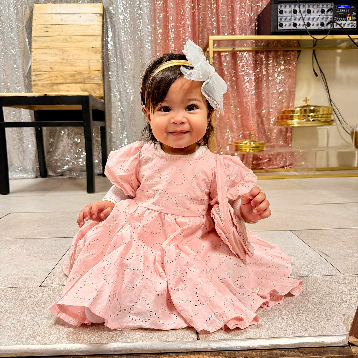 Amira Sophia is registered to the contest to win money with this photo: toddler, child, pink_dress, headband, bow, smile, sitting, floor, indoor, curtains, sparkle, wooden_chair, metal_shelf, golden_objects, happy, portrait, cute, baby, person, clothing