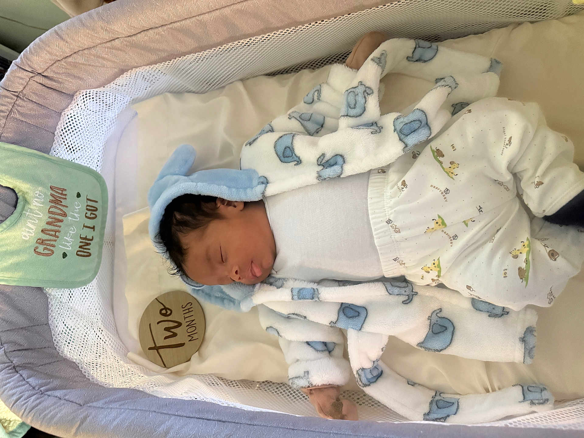 Owen is registered to the contest to win money with this photo: baby, sleeping, bassinet, blanket, clothing, elephant_pattern, infant, newborn, person, portrait, sleepwear, soft_toys, textile, white_background, blue, cute, cozy, baby_bib, baby_pants, indoors