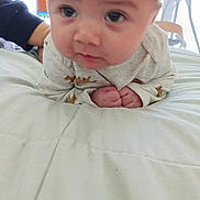 Jonathon is registered to the contest to win money with this photo: baby, infant, child, portrait, face, eyes, curious, serious, sitting, lying_down, onesie, clothing, hands, fists, bed, bedding, bedroom, adult, indoor, photography
