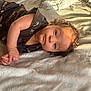 baby, bedroom, blanket, child, clothing, curly_hair, cute, fabric, face, hand, indoor, infant, light_shadow, looking_at_camera, lying_down, patterned_clothing, portrait, skin, soft, toddler