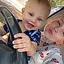 baby, child, woman, car, steering_wheel, smiling, happy, tattoos, nose_ring, short_sleeve, blue_eyes, outdoor, daylight, casual_clothing, portrait, family, cute, hand, person, vehicle_interior