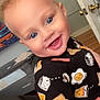 toddler, child, smiling, blue_eyes, curly_hair, blonde_hair, indoors, crib, playful_clothing, breakfast_pattern, milk_carton, fried_egg, toast, happy, person, portrait, room, door, colorful_art, cozy