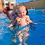 child, toddler, adult, pool, water, swimming, blue_eyes, curly_hair, red_hair, sunlight, outdoor, happy, smiling, holding, splash, summer, fun, family, play, leisure