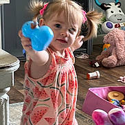Athena joined the competition — help win amazing prizes! toddler, child, toy, pink_hair_ties, dress, watermelon_pattern, stuffed_animals, blue_toy, floor, wooden_floor, indoor, playtime, curious, pigtails, pink, purple, container, pill_bottle, furniture, candid