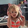 toddler, headphones, cat_ears, child, indoor, striped_dress, blonde_hair, living_room, toy, shelf, television, carpet, furniture, person, cute, curious, colorful_clothing, playful, home, portrait