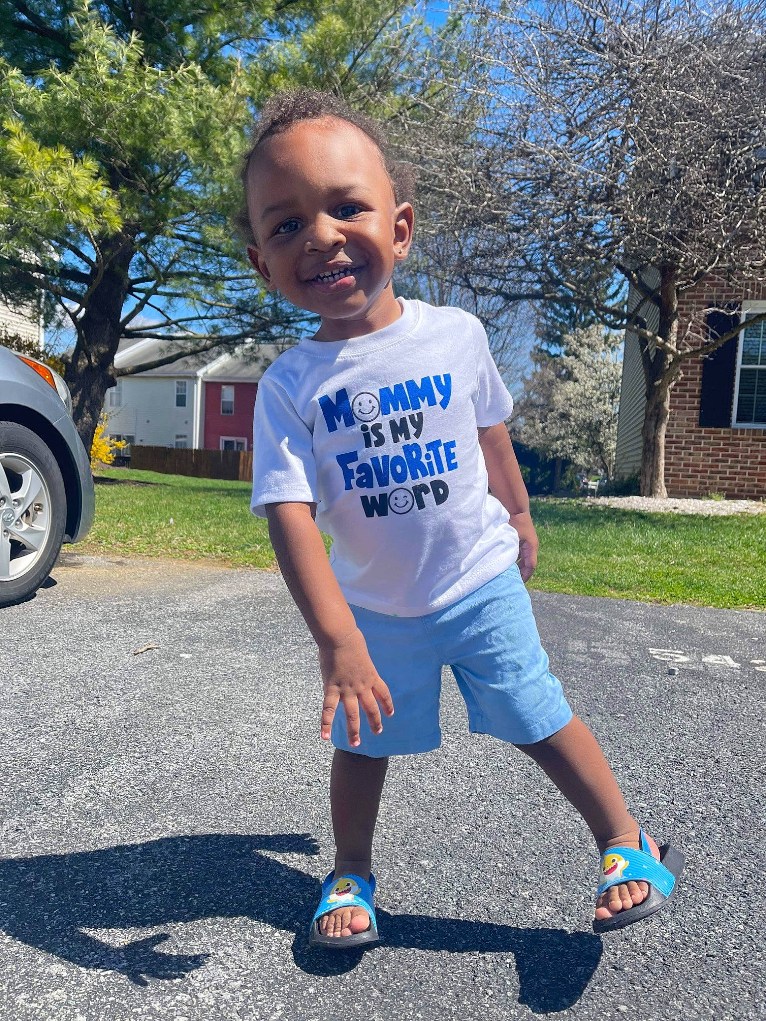 Josiah is registered to the contest to win money with this photo: asphalt, blue, cool, grass, happy, head, joy, leg, leisure, person, plant, public_space, shorts, sleeve, sportswear, standing, style, t_shirt, tire, tree