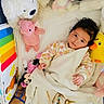 Victoria is registered to the contest to win money with this photo: baby, child, blanket, stuffed_animal, toy, plush_toy, yellow_duck, pink_bear, white_bear, mickey_mouse, crib, soft_toys, curly_hair, indoor, cute, infant, resting, colorful, comfort, peaceful