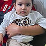 toddler, child, person, face, sweater, leopard_print, pants, sitting, indoor, hand, arm, couch, expression, cute, young, portrait, holding, clothing, comfort, casual