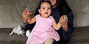 Angel is registered to the contest to win money with this photo: woman, toddler, child, pink_dress, tights, white_shoes, couch, living_room, clocks, easter_decorations, home_interior, holding_hands, smiling, family, indoor, carpet, plush, person, seated, cute