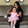 woman, toddler, child, pink_dress, tights, white_shoes, couch, living_room, clocks, easter_decorations, home_interior, holding_hands, smiling, family, indoor, carpet, plush, person, seated, cute