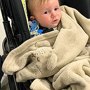 Ezio a rejoint le concours — aidez-le/la à gagner de superbes lots ! baby, blanket, bear_design, black_stroller, child, clip, curious, face, indoor, pacifier, person, plush, portrait, seated, soft_texture, toddler, transport, warm, young_child, wrapped
