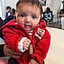 Francesca is registered to the contest to win money with this photo: baby, infant, child, face, eyes, red_hoodie, zipper, hand, portrait, close_up, cafe, table, number_33, people, background, seat, indoor, clothing, person, smile