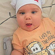 Viktor joined the competition — help win amazing prizes! baby, child, chef_hat, cute, cartoon_tshirt, peach_shirt, blue_eyes, lying_down, blanket, bed, smiling, open_mouth, infant, soft_toys, patterned_sheets, hand, expression, headwear, indoors, person
