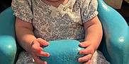Athena is registered to the contest to win money with this photo: baby, child, infant, blue_chair, floral_outfit, socks, hands, face, eyes, living_room, couch, cushion, carpet, indoor, seated, curious_expression, molded_chair, person, cute, young_child