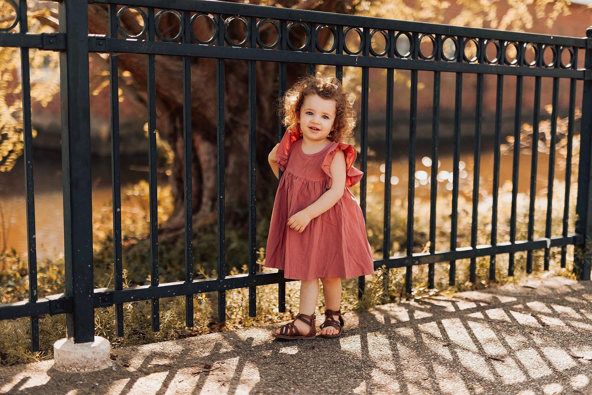 Charlotte is registered to the contest to win money with this photo: bridge, child, dress, fence, fun, grass, guard_rail, happy, joy, leisure, magenta, metal, pattern, people_in_nature, person, plant, sandal, sky, toddler, tree