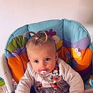 Maïna participe au concours pour gagner de l'argent avec cette photo : baby, blonde_hair, blue_eyes, cartoon, child, clothing, colorful, cute, high_chair, indoor, infant, pacifier, person, playful_hairstyle, portrait, seat, smiling, toddler, toy, young_child