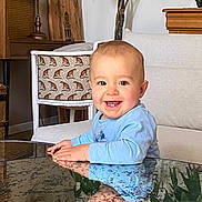 Pio a rejoint le concours — aidez-le/la à gagner de superbes lots ! baby, child, smile, reflection, glass_table, blue_shirt, indoor, living_room, furniture, plant, chair, cute, happy, portrait, face, hands, wooden_furniture, home_decor, infant, person