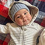baby, infant, child, face, hoodie, beanie, hat, striped_clothing, blanket, patchwork, cozy, cute, portrait, lying_down, indoor, warm_clothing, expression, chubby_cheeks, closeup, young
