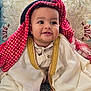 Adnan a rejoint le concours — aidez-le/la à gagner de superbes lots ! baby, child, smile, traditional_clothing, headscarf, red, white, gold_trim, sitting, sofa, patterned_fabric, cute, indoors, portrait, happy, face, feet, young, cultural, infant