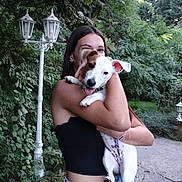 Zigzag participe au concours pour gagner de l'argent avec cette photo : dog, puppy, person, woman, outdoor, garden, greenery, trees, leaves, lantern, portrait, hugging, smiling, tongue_out, white_and_brown, pet, animal, arms, pathway, daylight