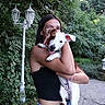dog, puppy, person, woman, outdoor, garden, greenery, trees, leaves, lantern, portrait, hugging, smiling, tongue_out, white_and_brown, pet, animal, arms, pathway, daylight