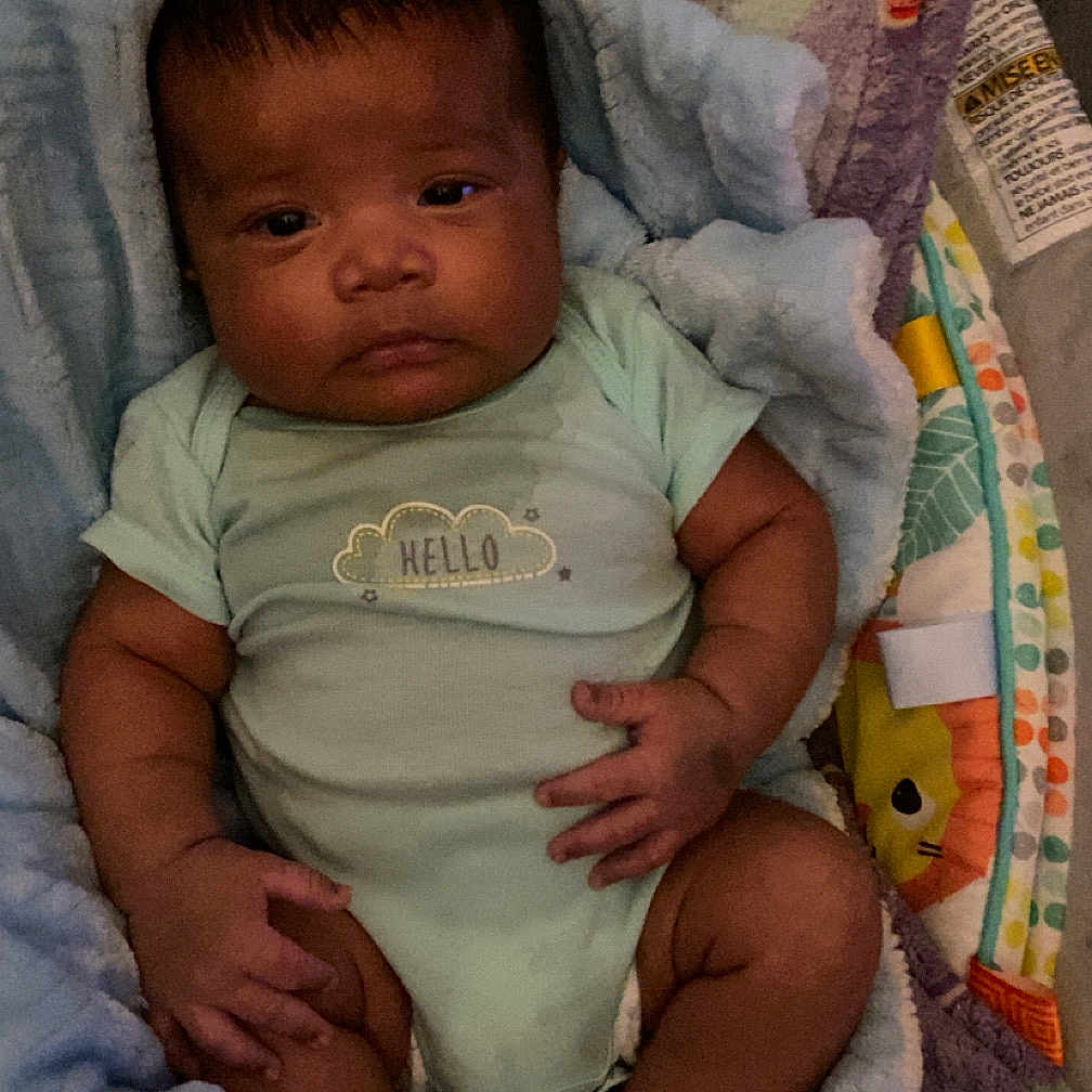 Makaio is registered to the contest to win money with this photo: baby, blanket, child, clothing, comfort, cozy, cute, expression, face, foot, hand, indoors, infant, newborn, onesie, person, portrait, sitting, skin, soft_texture