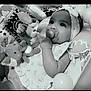 baby, black_and_white, child, closeup, curious, cute, dress, elephant_toy, face, hand, headband, indoor, infant, lying_down, pacifier, patterned, playmat, smiling, soft_toy, toy
