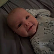 Ivory is registered to the contest to win money with this photo: baby, infant, smile, face, bed, blanket, onesie, animal_print, cute, child, portrait, indoors, soft_lighting, happy, young, person, lying_down, apparel, cozy, comfort