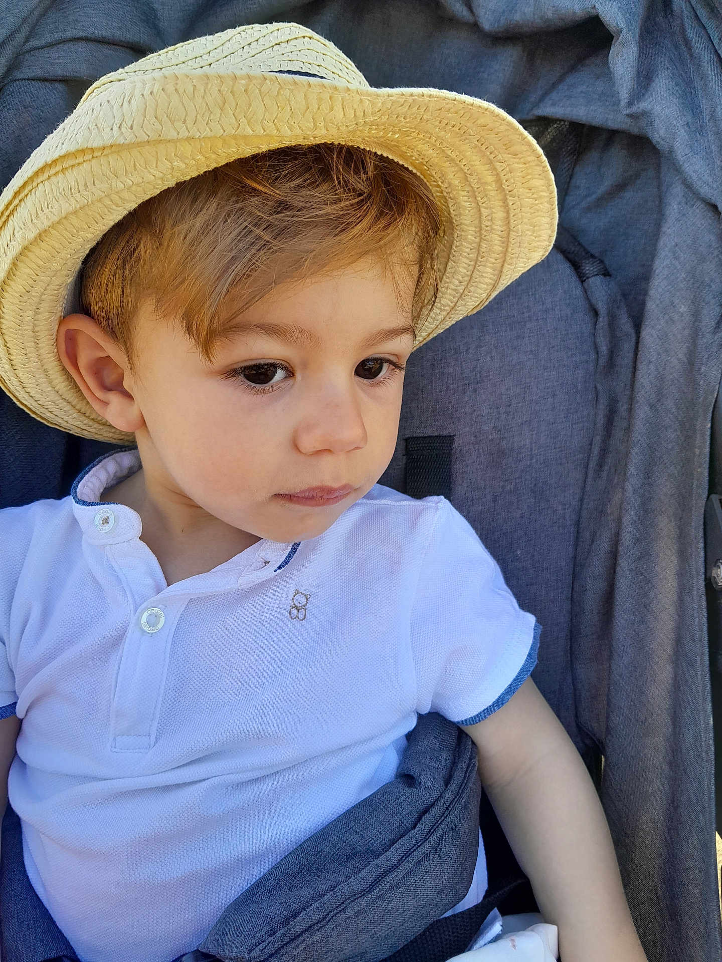 Gabriele a rejoint le concours — aidez-le/la à gagner de superbes lots ! toddler, child, hat, straw_hat, white_shirt, stroller, seatbelt, curious, portrait, young_child, outdoor, casual_clothing, baby, face, person, headwear, summer, cute, sitting, looking_away