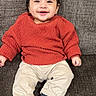 Aliyan is registered to the contest to win money with this photo: baby, child, smiling, sitting, red_sweater, beige_pants, blue_shoes, couch, indoor, happy, portrait, cute, infant, person, fashion, footwear, clothing, young_child, cozy, casual