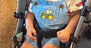 Aliyan is registered to the contest to win money with this photo: toddler, child, stroller, denim_overalls, curly_hair, smiling, white_socks, shoes, patterned_fabric, indoor, seat_belt, cute, happy, baby, portrait, clothing, playful, infant, person, cute_expression