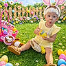 Kalani joined the competition — help win amazing prizes! toddler, child, bunny_ears, yellow_outfit, easter_eggs, grass, basket, plush_toy, flowers, wooden_fence, bunting, outdoor, spring, candy, headband, surprised_expression, sandals, sky, greenery, playful