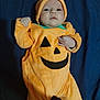 baby, infant, costume, pumpkin, orange, cute, child, portrait, lying_down, clothing, hat, smile, face, hand, fabric, blanket, indoor, soft, holiday, halloween