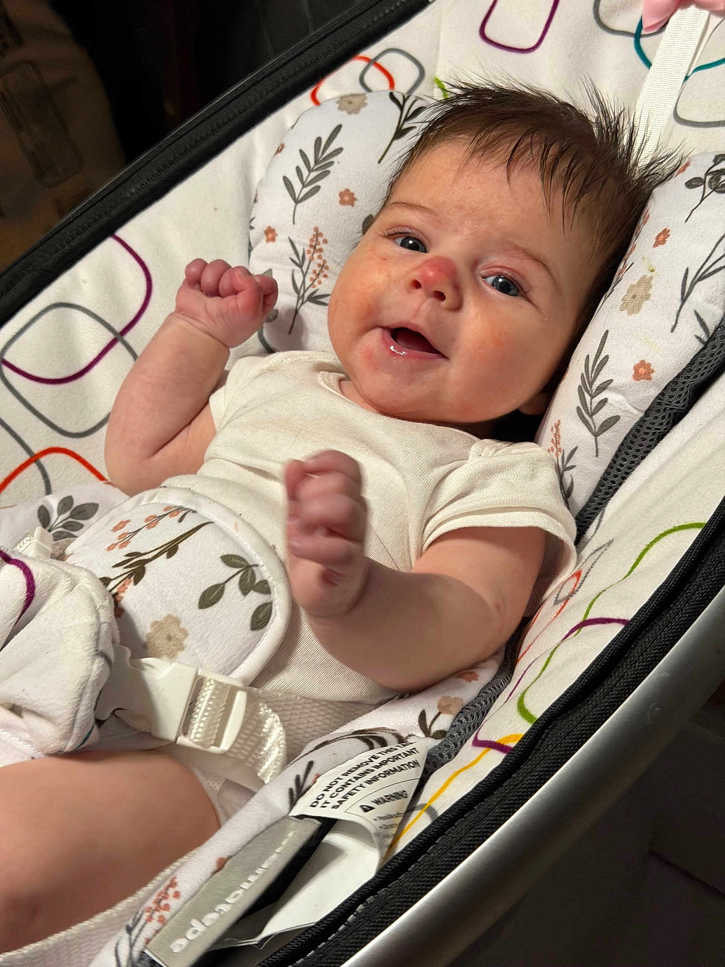 Emilia is registered to the contest to win money with this photo: baby, infant, smiling, happy, face, arms, clothing, seat, baby_seat, pattern, floral, white_clothing, comfort, indoor, child, cute, portrait, skin, person, expression