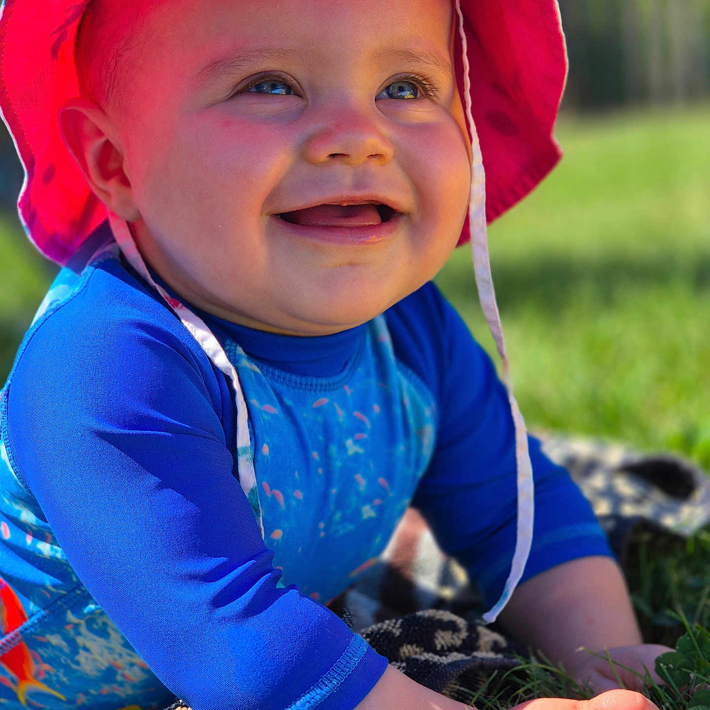 Nina a rejoint le concours — aidez-le/la à gagner de superbes lots ! baby, blue_clothing, cheeks, child, closeup, cute, daylight, face, grass, hands, happy, hat, infant, nature, outdoor, portrait, smiling, sunhat, sunlight, towel