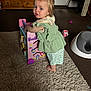 Evelyn joined the competition — help win amazing prizes! toddler, child, toy, walker, carpet, barefoot, hair_clip, green_clothing, indoor, living_room, furniture, cabinet, cup, potty, curious, standing, floor, playtime, young_child, home