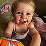 toddler, child, smiling, blue_eyes, blond_hair, indoor, carpet, toy, blanket, pink_clothing, happy, face, person, cute, playful, close_up, baby, skin, expression, arm
