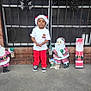 bars, brick_wall, child, concrete_floor, cute, festive, holiday_decorations, holiday_spirit, outdoor, red_pants, reindeer, santa_claus, santa_hat, seasonal, smiling, sneakers, standing, white_tshirt, window, winter