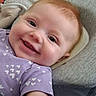 baby, child, smile, face, red_hair, purple_clothing, heart_pattern, cushion, closeup, happy, infant, portrait, person, skin, eyes, mouth, cheeks, lying_down, indoors, soft_fabric