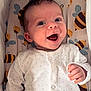 baby, infant, smiling, happy, onesie, white_clothing, patterned_background, bee_pattern, cute, child, face, hand, portrait, lying_down, indoor, soft_lighting, newborn, closeup, expression, joy