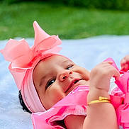 Aaina joined the competition — help win amazing prizes! baby, pink_bow, headband, smiling, outdoor, green_background, blanket, golden_bracelet, infant, cute, happy, portrait, child, soft_texture, closeup, baby_clothing, toddler, playful, young_child, natural_light