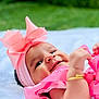 baby, pink_bow, headband, smiling, outdoor, green_background, blanket, golden_bracelet, infant, cute, happy, portrait, child, soft_texture, closeup, baby_clothing, toddler, playful, young_child, natural_light