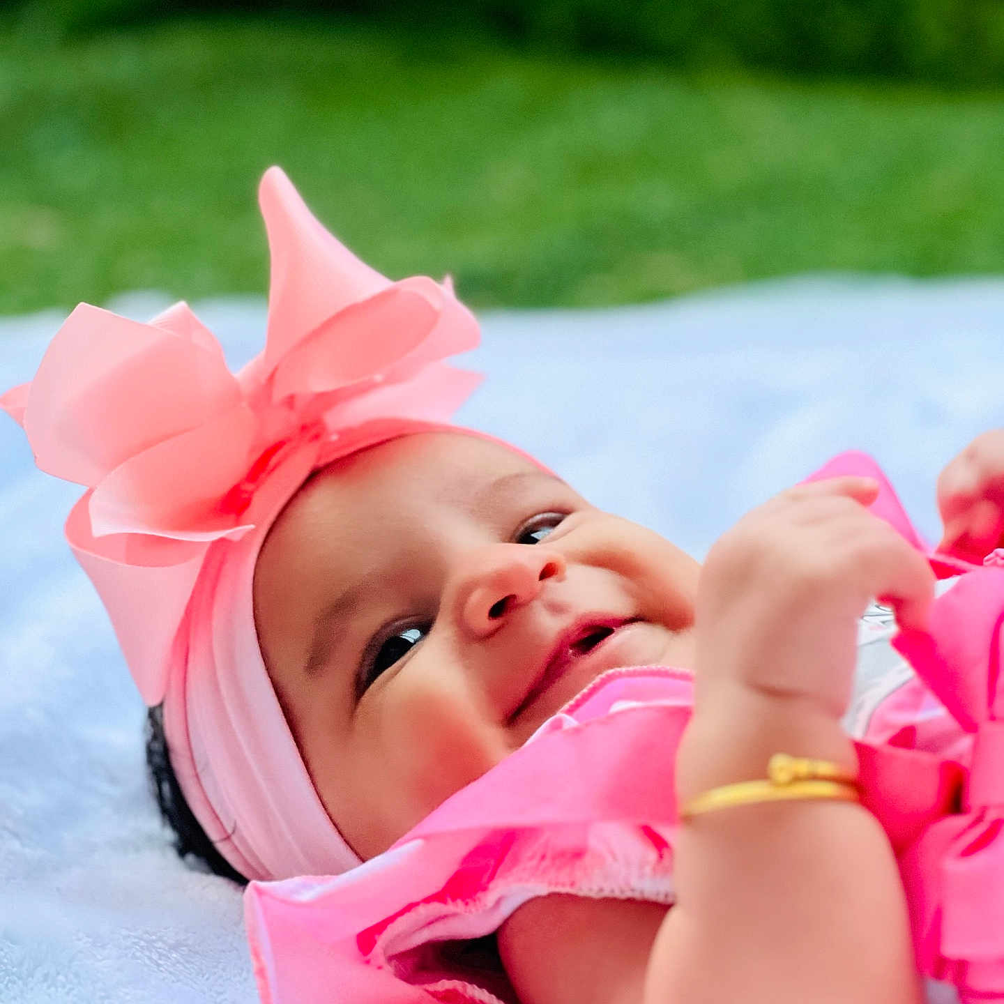 Aaina joined the competition — help win amazing prizes! baby, baby_clothing, blanket, child, closeup, cute, golden_bracelet, green_background, happy, headband, infant, natural_light, outdoor, pink_bow, playful, portrait, smiling, soft_texture, toddler, young_child