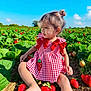 Duaa is registered to the contest to win money with this photo: toddler, child, dress, red_bow, strawberry, field, green_leaves, outdoor, sunny, blue_sky, plant, nature, cute, sitting, portrait, young_child, daylight, garden, fruit, happy
