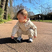 Sebastian participe au concours pour gagner de l'argent avec cette photo : child, toddler, baby, squatting, stick, pavement, park, trees, sunny, outdoors, sneakers, hoodie, playing, exploring, bicycle, background_person, shadow, face, nature, casual_clothing