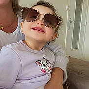 Lyna a rejoint le concours — aidez-le/la à gagner de superbes lots ! toddler, child, sunglasses, smile, indoor, sweater, cat_graphic, jeans, adult, hand, couch, door, window, portrait, happy, curly_hair, casual_clothing, person, accessory, family
