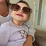 toddler, child, sunglasses, smile, indoor, sweater, cat_graphic, jeans, adult, hand, couch, door, window, portrait, happy, curly_hair, casual_clothing, person, accessory, family