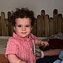baby, bed, child, cozy, curly_hair, cute, expression, face, furniture, hand, home, indoor, person, pink_clothing, portrait, smiling, toddler, wall_art, wooden_headboard, young_child