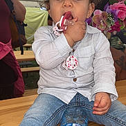 Inaïa a rejoint le concours — aidez-le/la à gagner de superbes lots ! toddler, child, pacifier, curly_hair, jeans, shirt, water_bottle, table, flower_arrangement, indoor, person, face, hand, foot, sitting, casual_clothing, curious, brown_eyes, skin, background