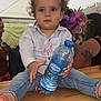 Inaïa participe au concours pour gagner de l'argent avec cette photo : child, toddler, curly_hair, water_bottle, table, jeans, shirt, indoor, people, flowers, pacifier, hand, face, eyes, nose, mouth, background, tent, casual_clothing, sitting